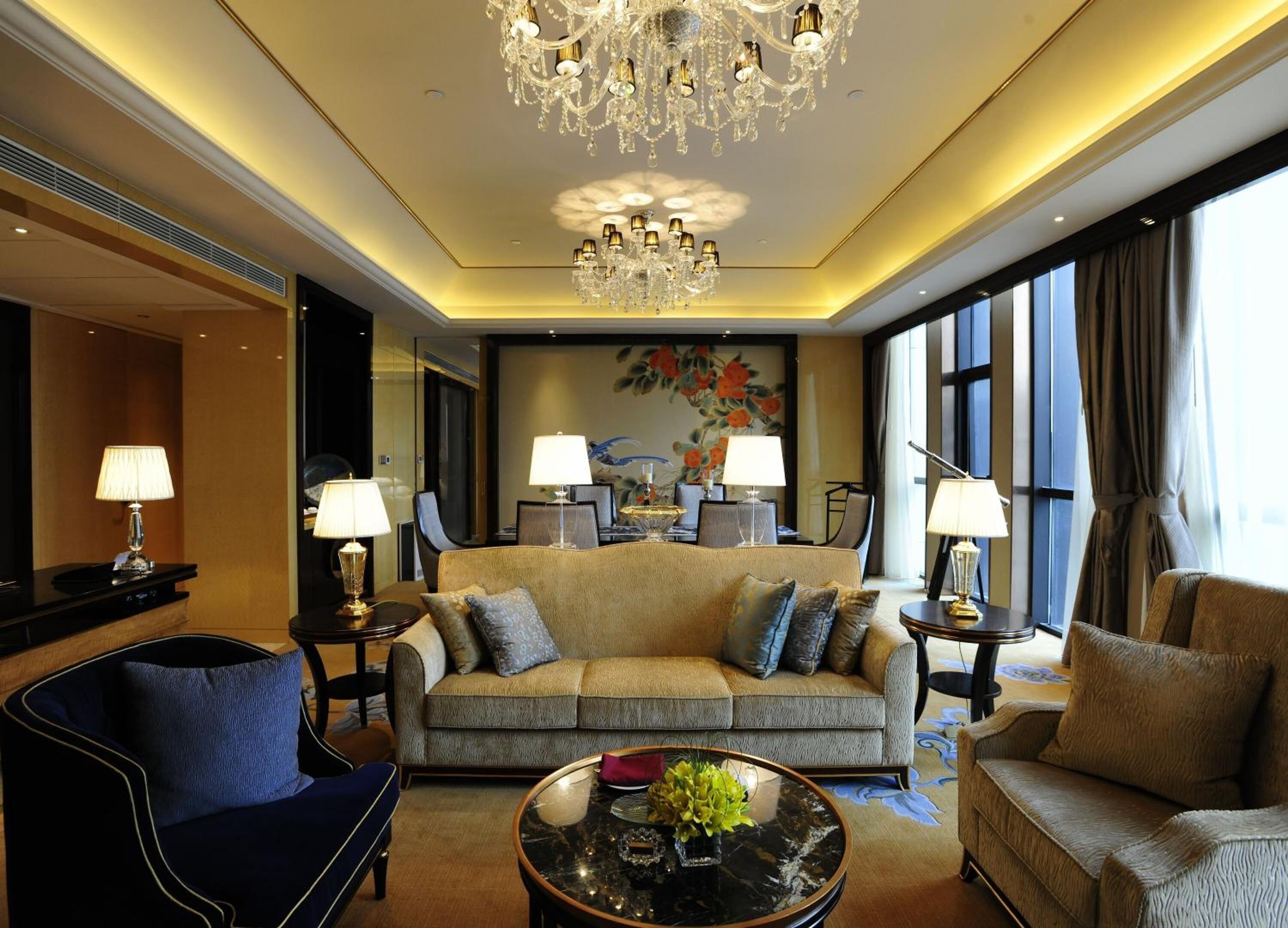 A luxurious hotel room with a large sofa, a round coffee table, and a chandelier.