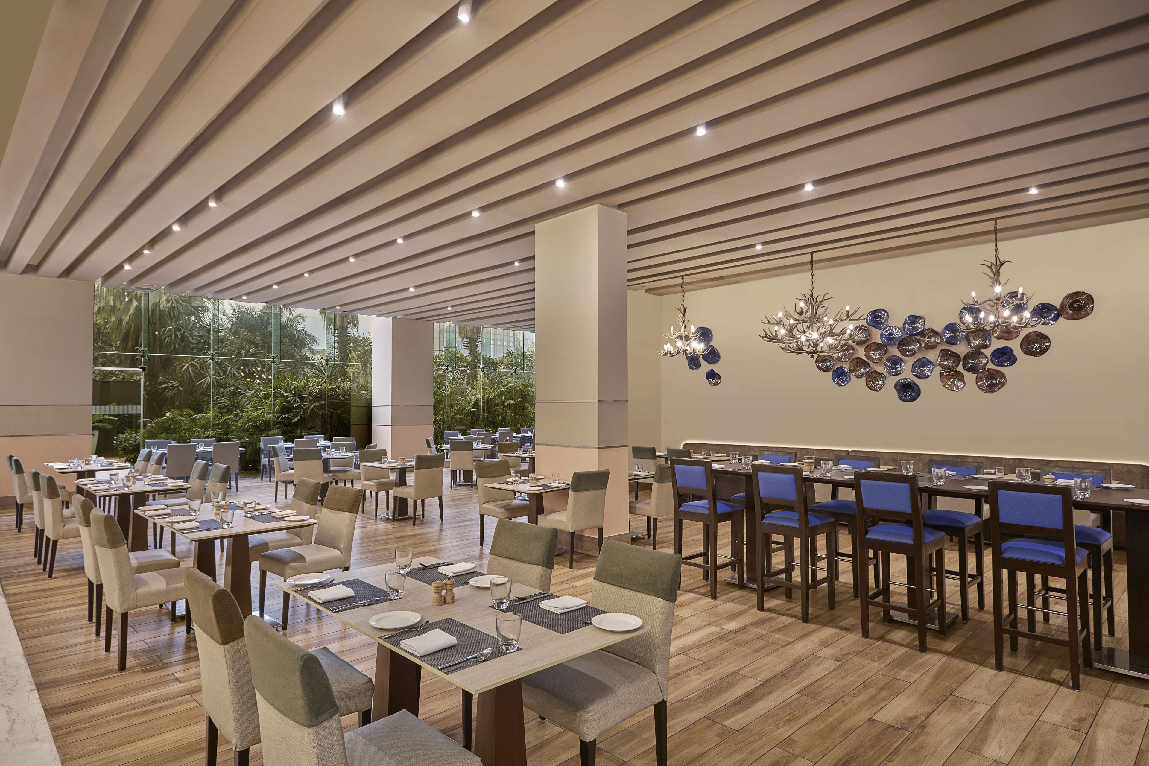 Un espace de restauration moderne, avec des tables et des chaises, un lustre et une vue sur la verdure environnante.