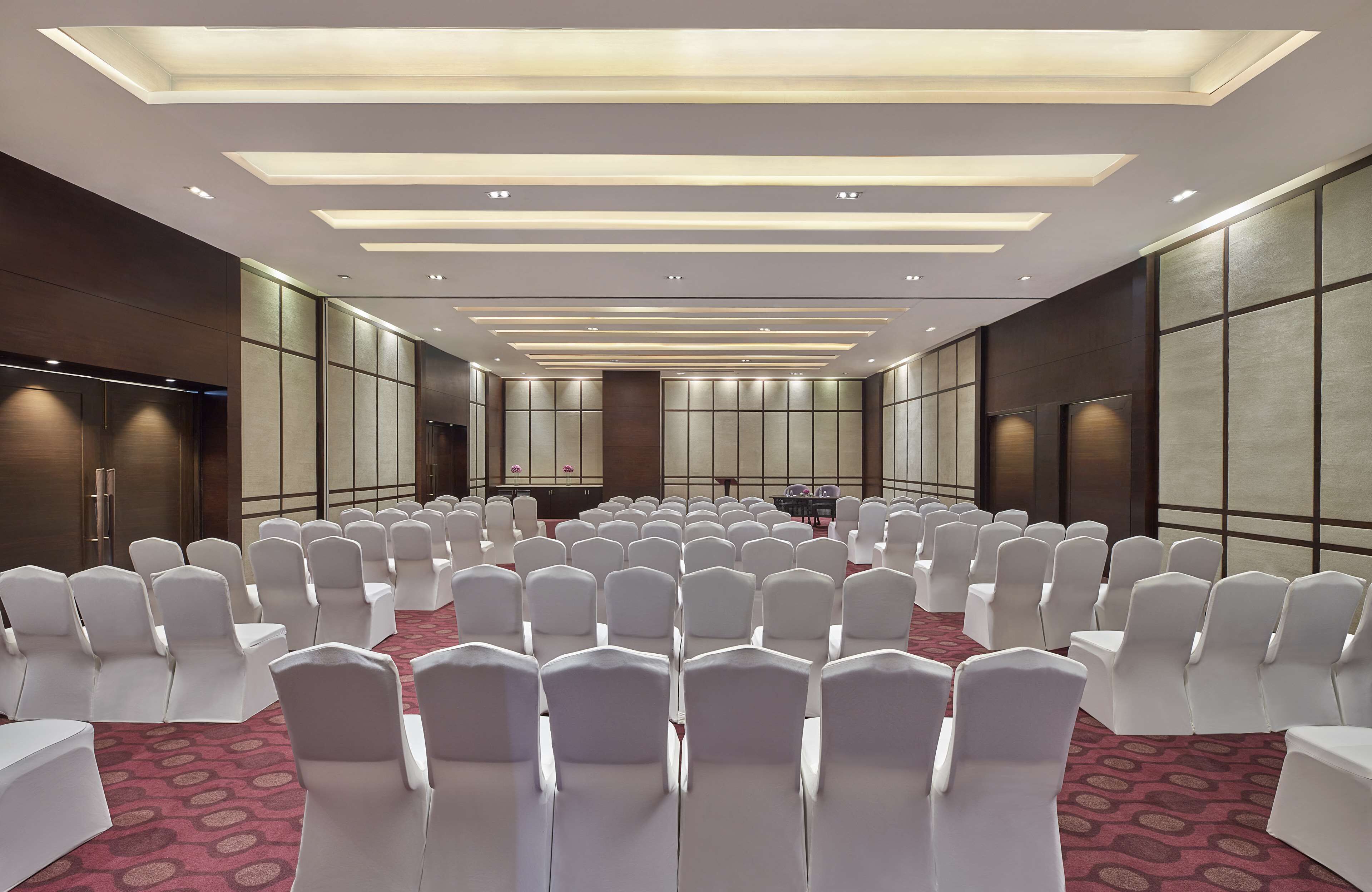 A conference room with rows of white chairs, a stage, and a modern ceiling design.
