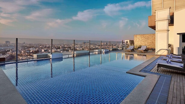 A rooftop infinity pool with a city view, lounge chairs, and a modern building facade. - DoubleTree by Hilton Gurugram Baani Square (Gurugram)