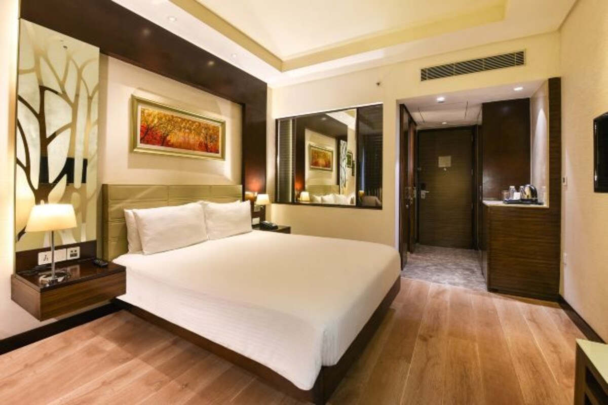 A hotel room with a large bed, a nightstand with a lamp, a mirror, and a painting on the wall.
