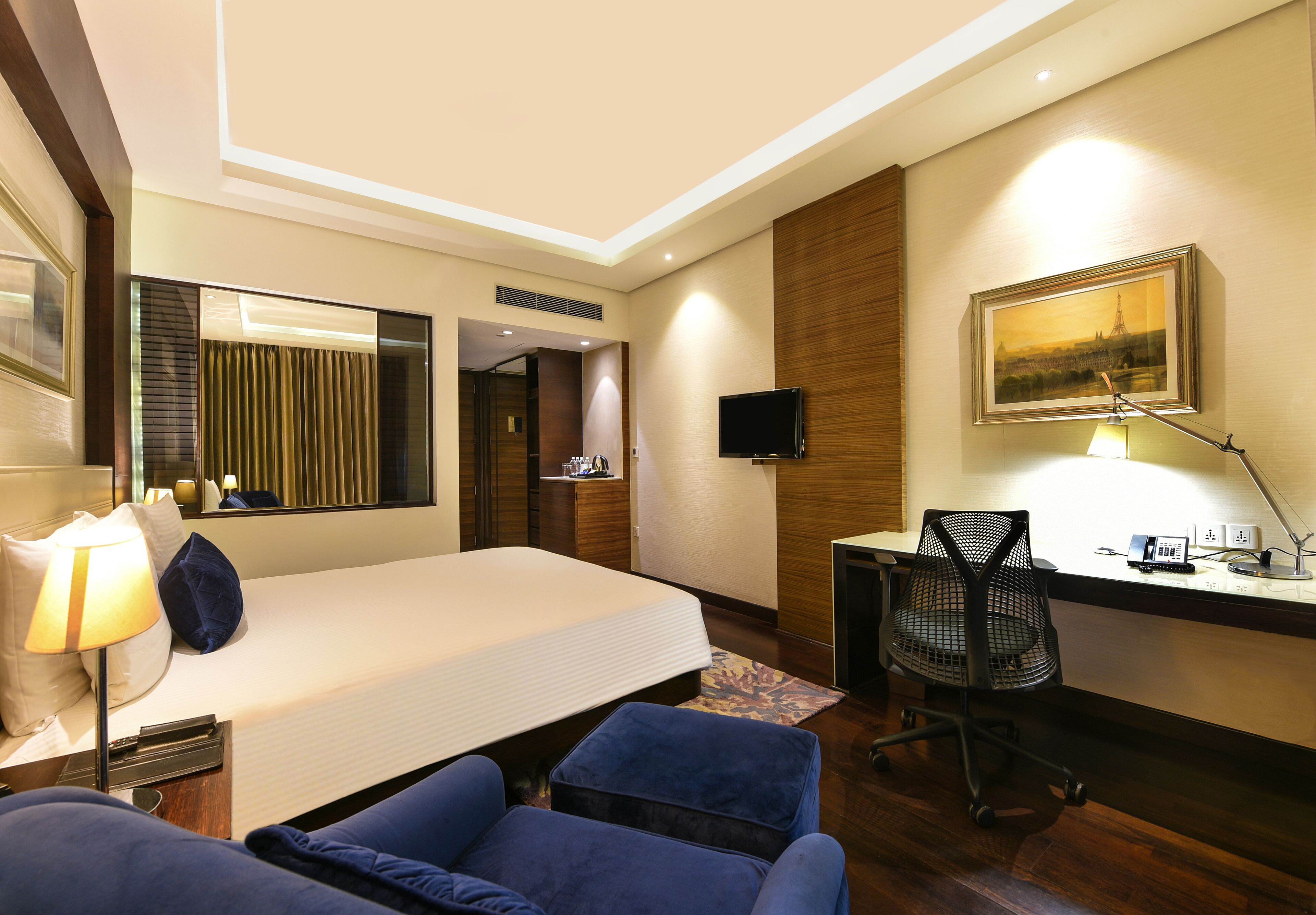 Ein Hotelzimmer mit Bett, Schreibtisch, Stuhl, Lampe, Fernseher und einem Bild an der Wand.