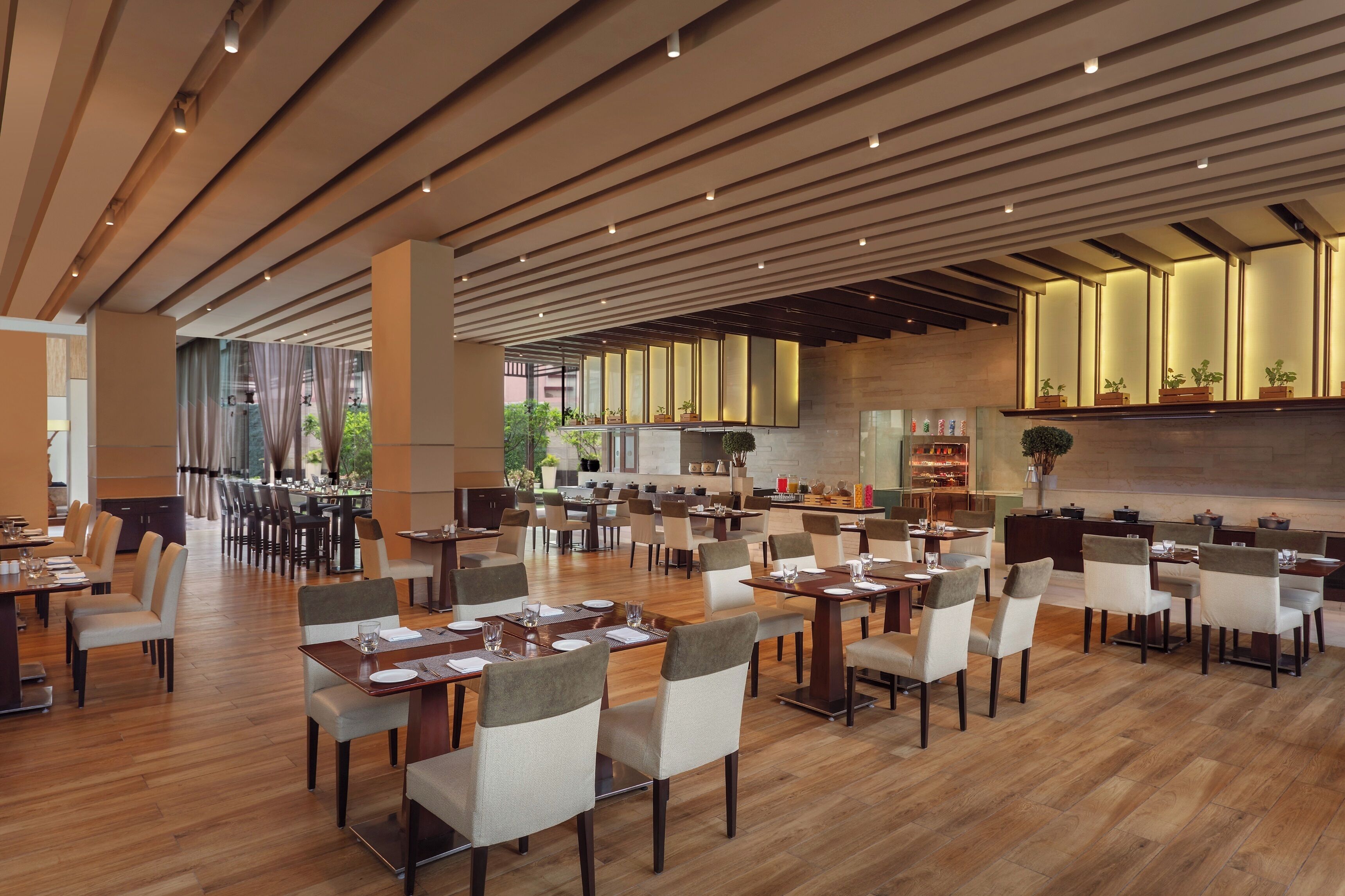 A spacious dining area with multiple tables and chairs, wooden flooring, and a modern ceiling design.