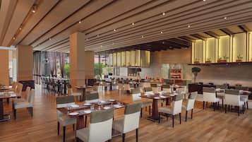 A spacious dining area with multiple tables and chairs, wooden flooring, and a modern ceiling design.