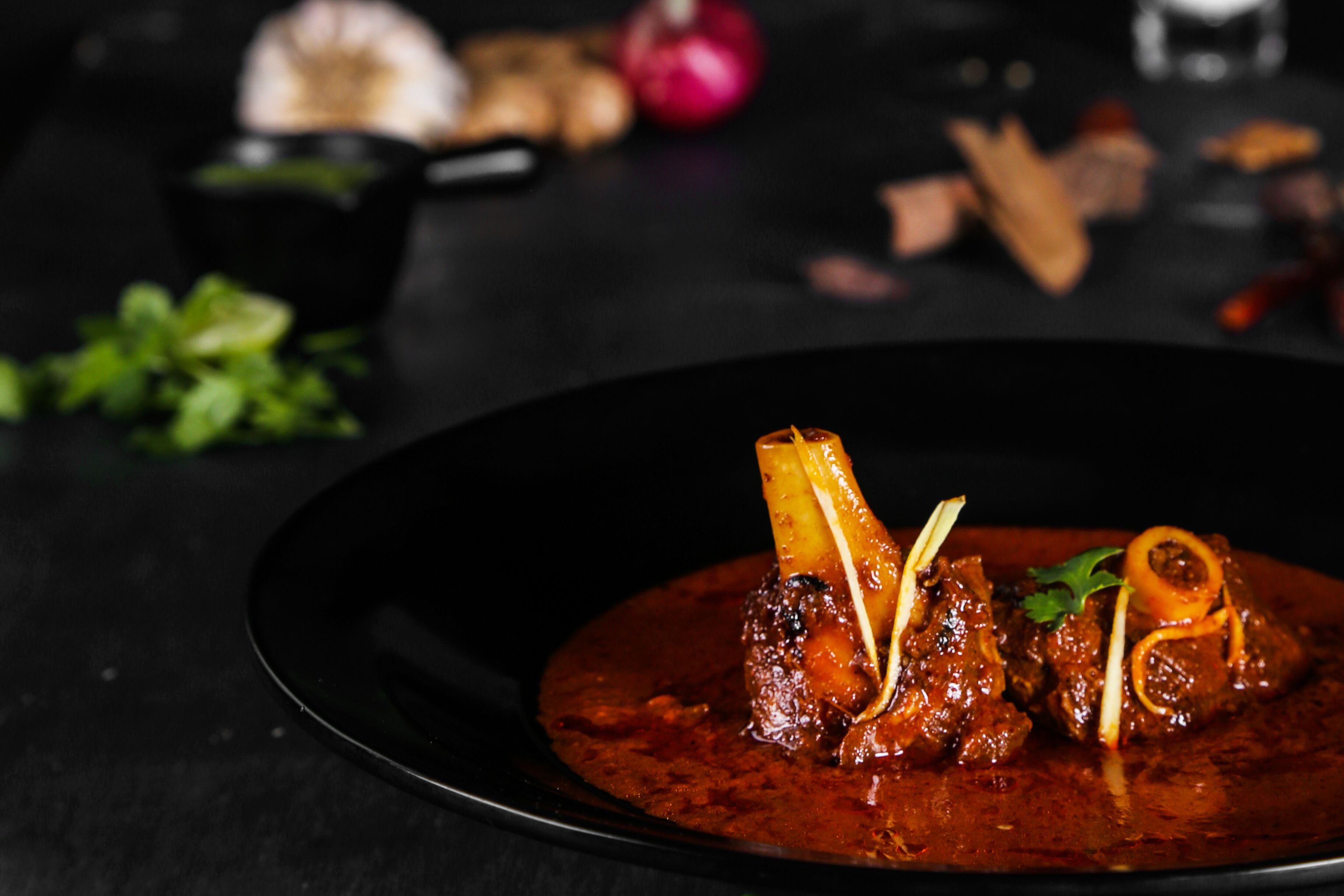 Un plat composé de viande et agrémenté de morceaux d’os, le tout présenté dans une assiette sombre.