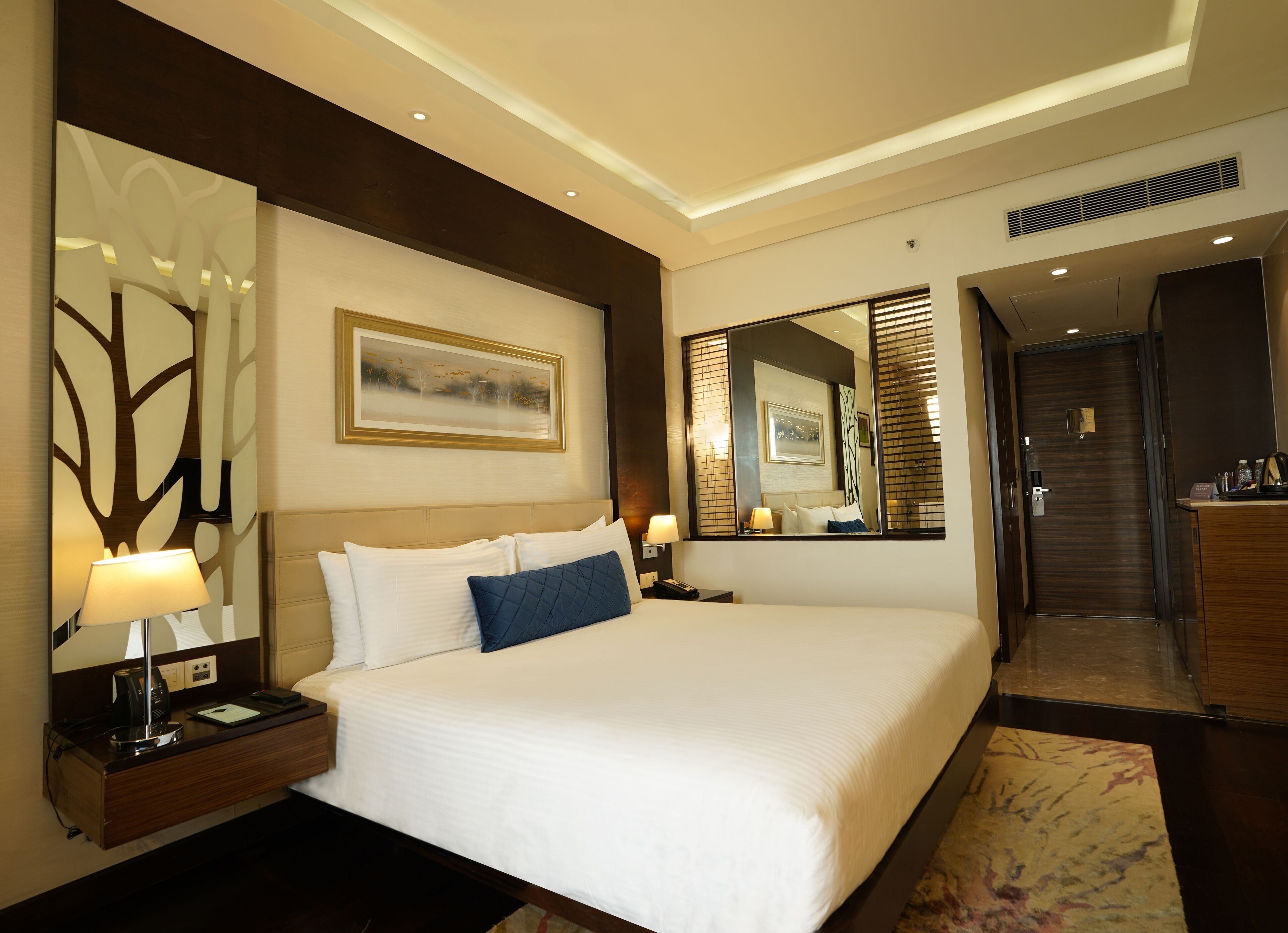 A hotel room with a large bed, bedside tables, a desk, and a mirror.