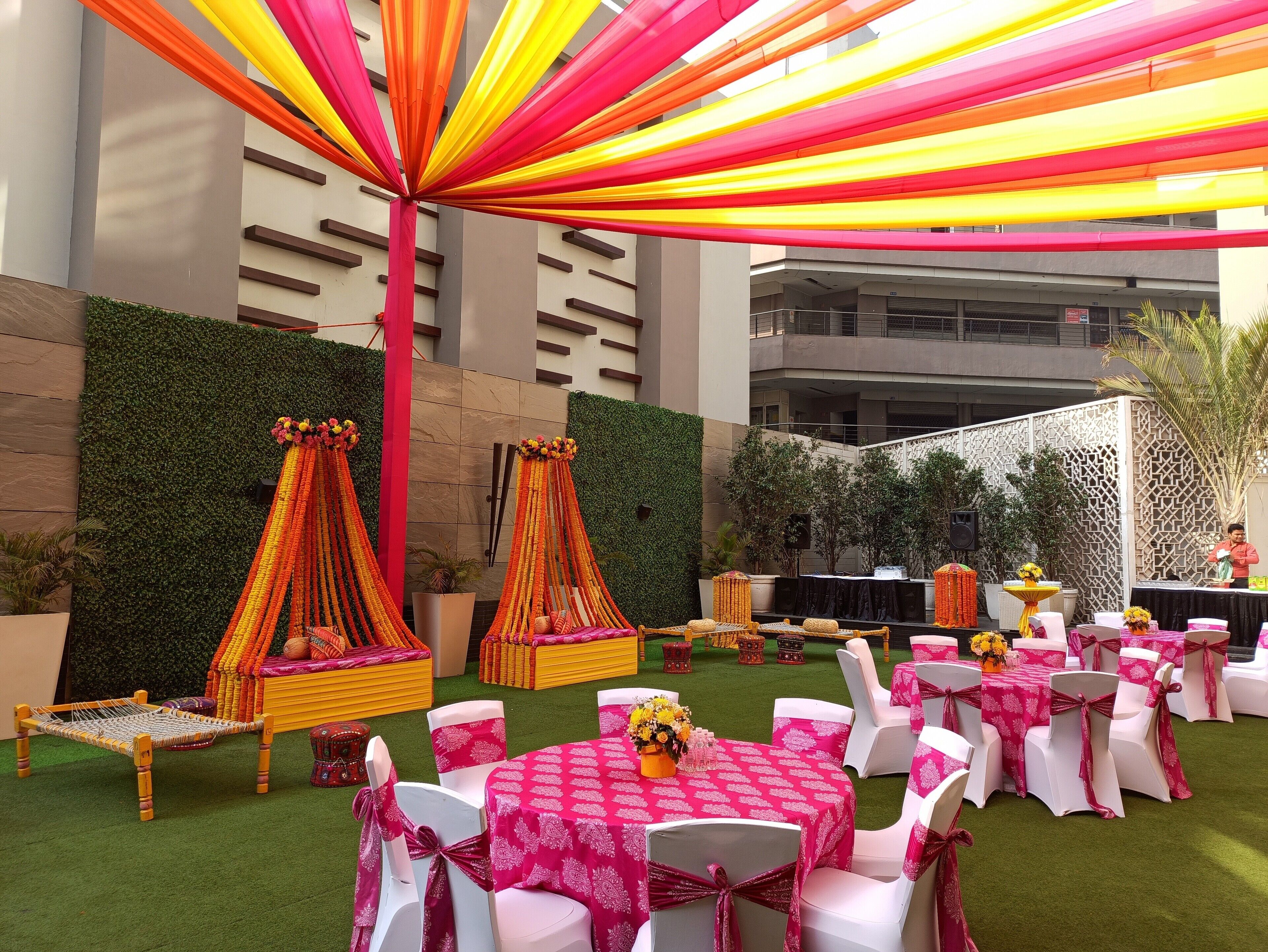 Een evenementenlocatie buiten met tafels, stoelen, een podium en decoratieve elementen zoals draperieën en bloemarrangementen.