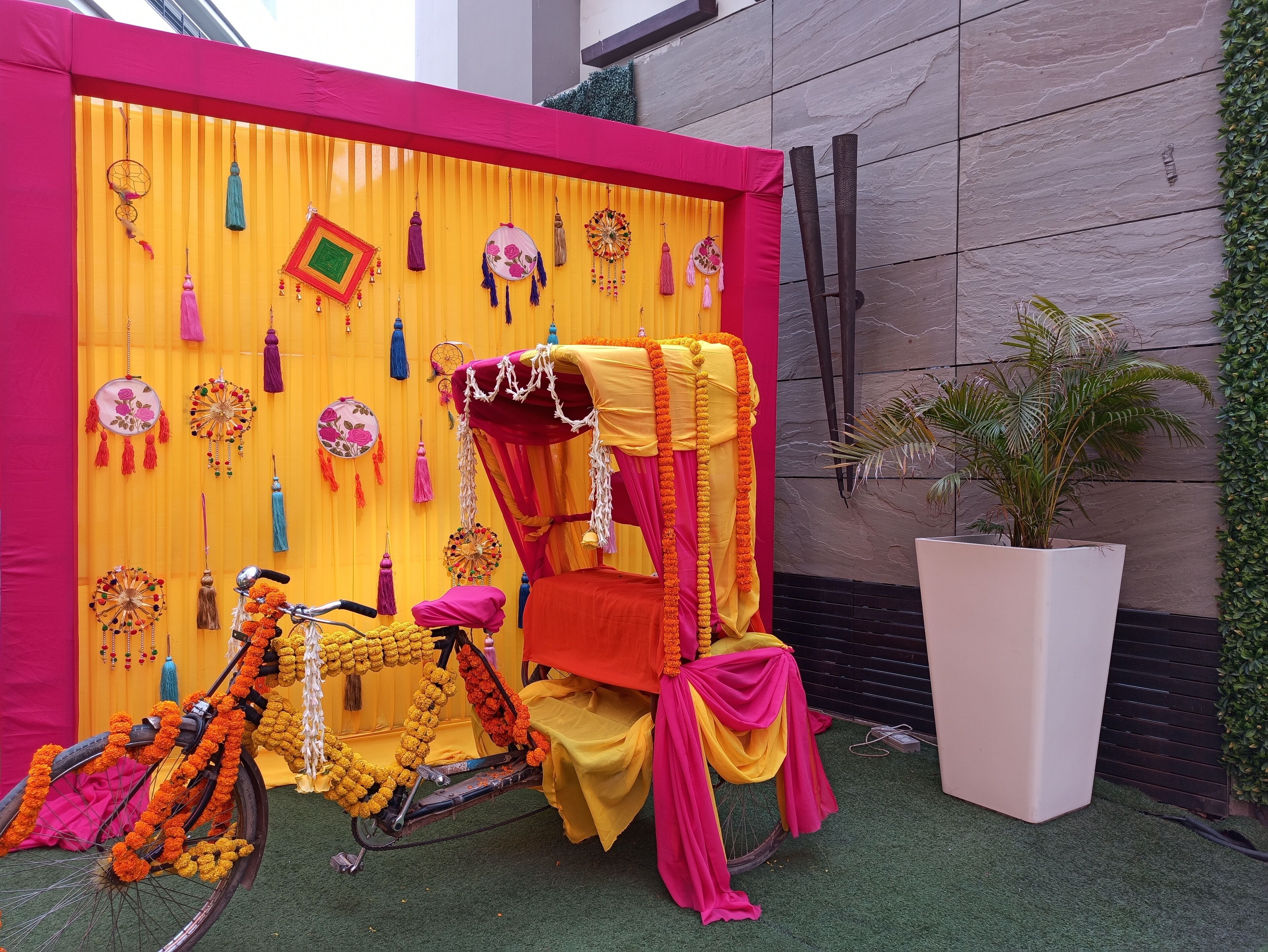 Una bicicleta decorada con un toldo y guirnaldas florales, sobre un fondo amarillo vibrante y adornos colgantes.