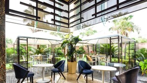 A modern indoor patio area with glass partitions, round tables, and dark chairs. - DoubleTree by Hilton Gurugram Baani Square (Gurugram)