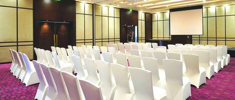 A conference room with rows of white chairs and a purple carpet.