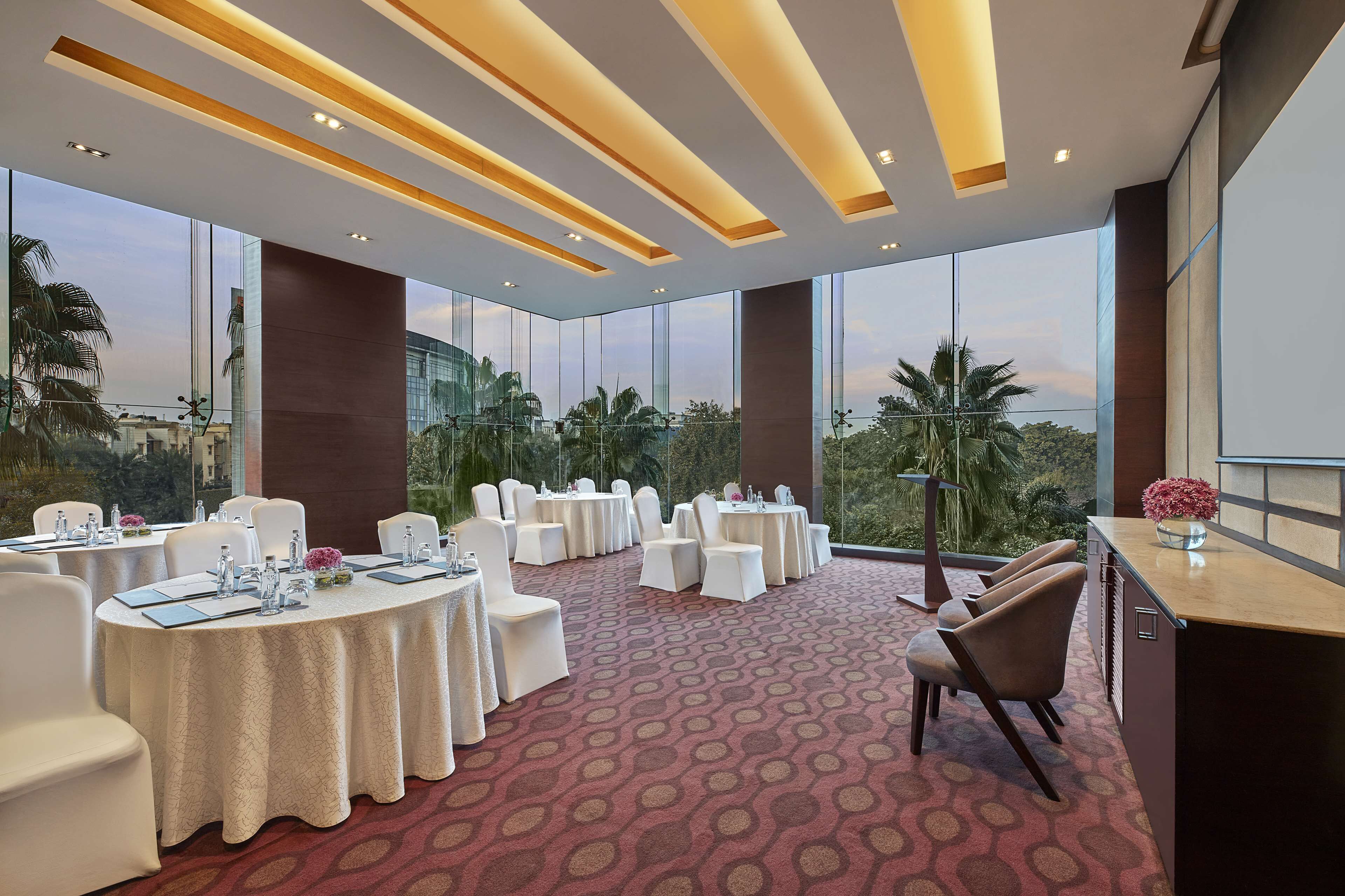 A conference room with round tables, white chairs, and a red patterned carpet.