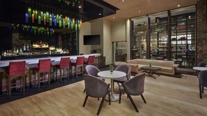 A modern bar area with a long counter, red chairs, and a seating area with round tables and purple chairs. - DoubleTree by Hilton Gurugram Baani Square (Gurugram)