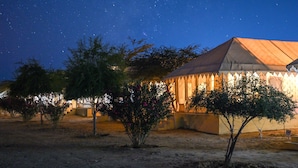 Un paisaje desértico nocturno con un edificio que tiene techo puntiagudo y una cerca decorativa.