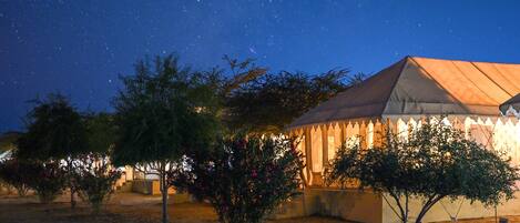 A desert landscape at night with a building featuring a pointed roof and a decorative fence.