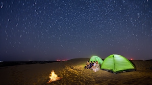 Campaamento en el desierto con dos tiendas de campaña y una fogata bajo un cielo estrellado.