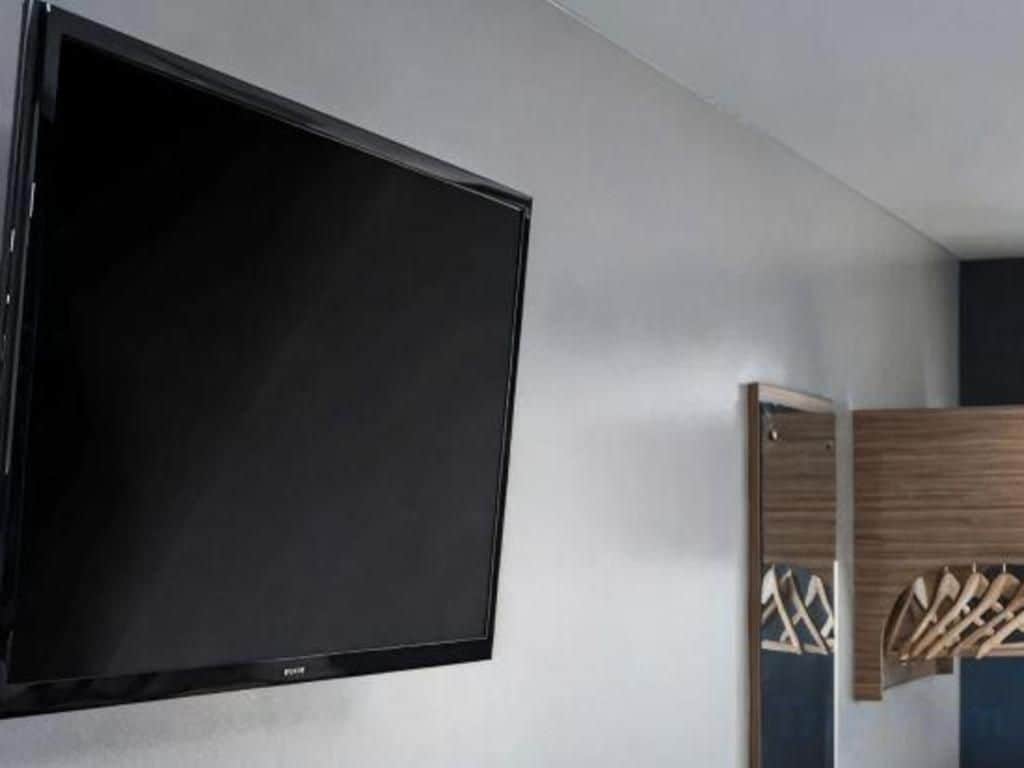 A flat-screen TV mounted on a wall, a wooden cabinet with hanging items, and a patterned wall design.