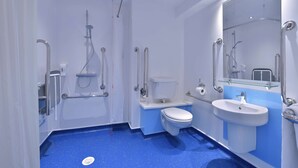 A modern bathroom with a shower, toilet, and sink, equipped with grab bars and a glass partition. - Travelodgellanelli Cross Hands (Llanelli)