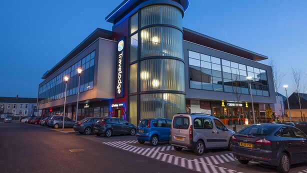 A modern building with a curved glass facade, a prominent 'Travelodge' sign, and a parking lot with several cars. - Travelodgellanelli Cross Hands (Llanelli)