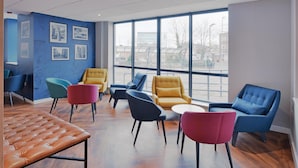 A modern waiting area with a large window, several colorful chairs, and a tufted bench. - Travelodge Woking Central (Woking)