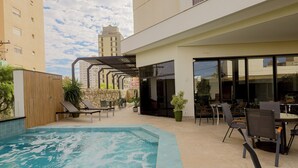 Un área de piscina moderna al aire libre con jacuzzi, sillones de descanso y un patio con mesas y sillas.