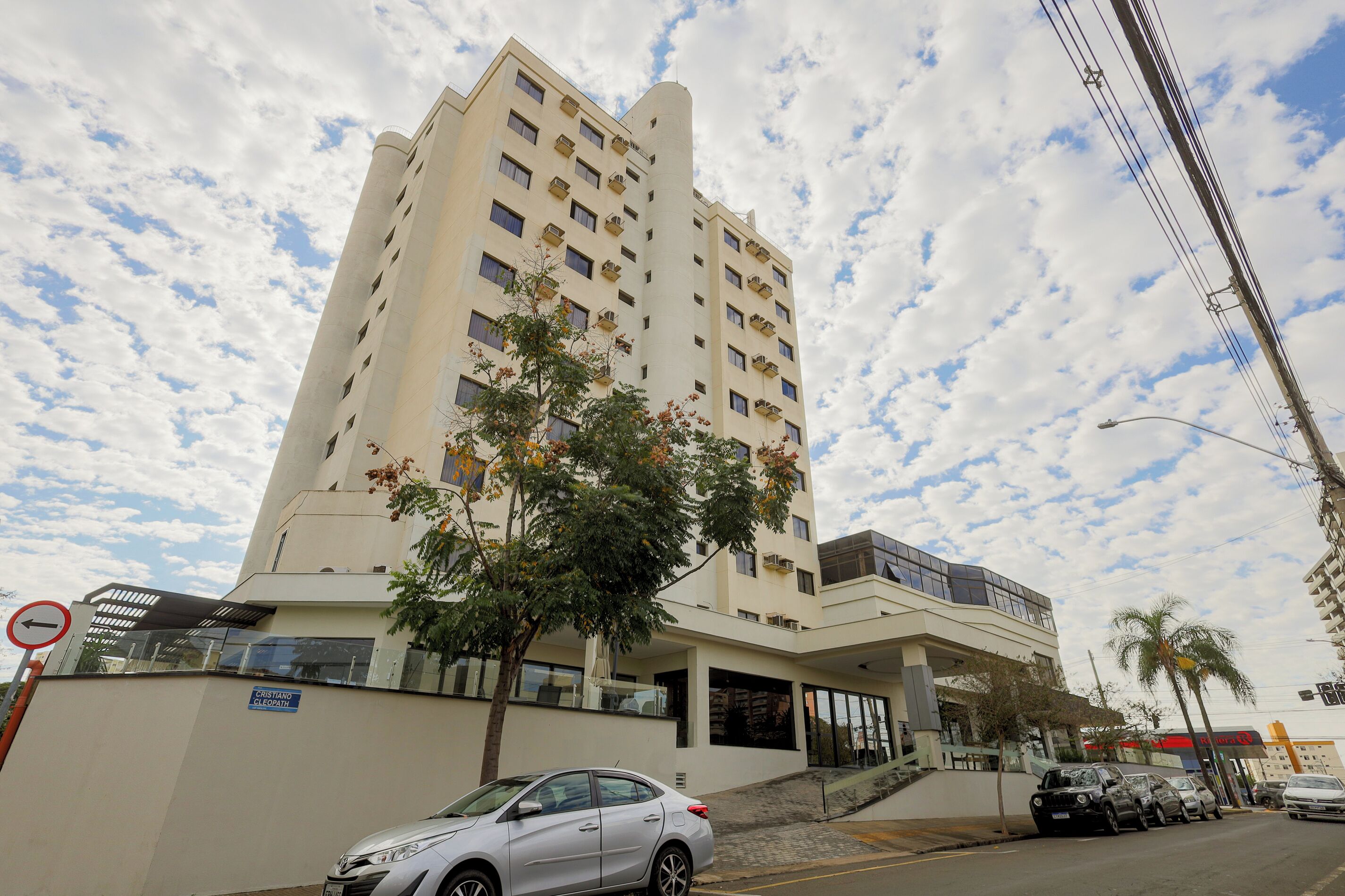 Un hotel de varios pisos con fachada plana, un acceso cubierto y una palmera frente a él.