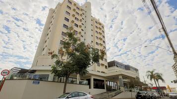 Un hotel de varios pisos con fachada plana, un acceso cubierto y una palmera frente a él.