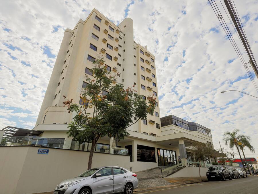 Un hotel de varios pisos con fachada plana, un acceso cubierto y una palmera frente a él.