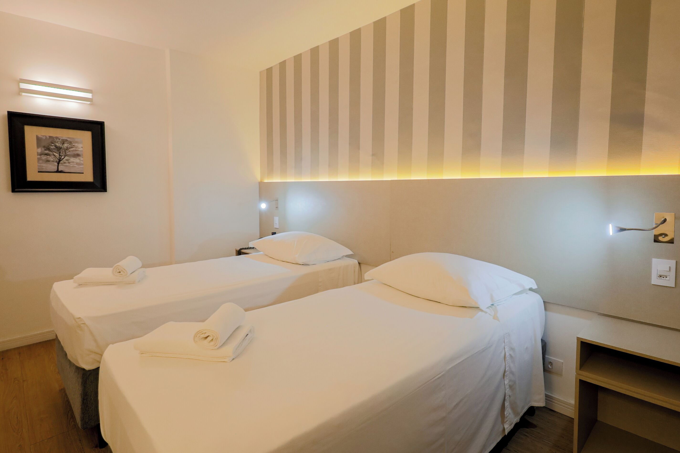 Hotellihuone, jossa on kaksi erillistä sänkyä. Jokaisessa sängyssä on valkoinen peitto ja tyyny, sekä yöpöytä ja seinään kiinnitetty valaisin.