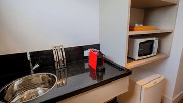 Una cocina compacta con un lavamanos de acero inoxidable, una cafetera roja, un microondas y un refrigerador pequeño.