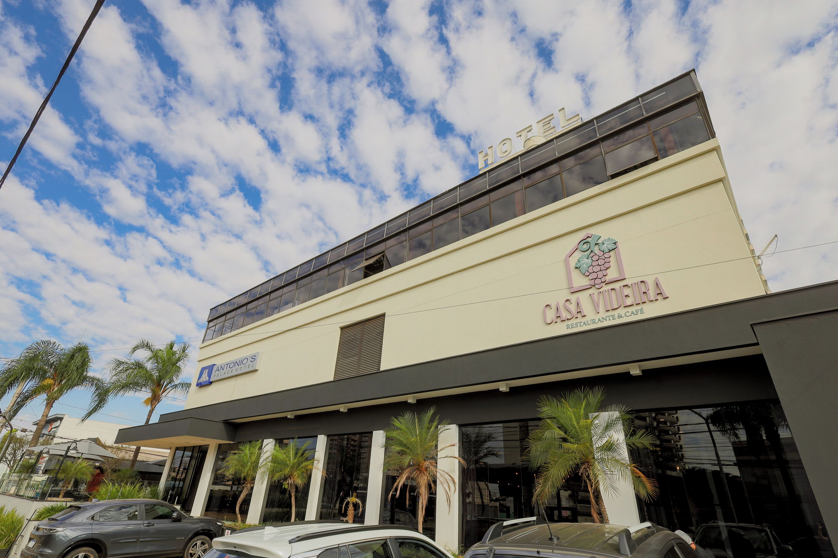 A hotel with a modern facade, palm trees in front, and a clear sky.