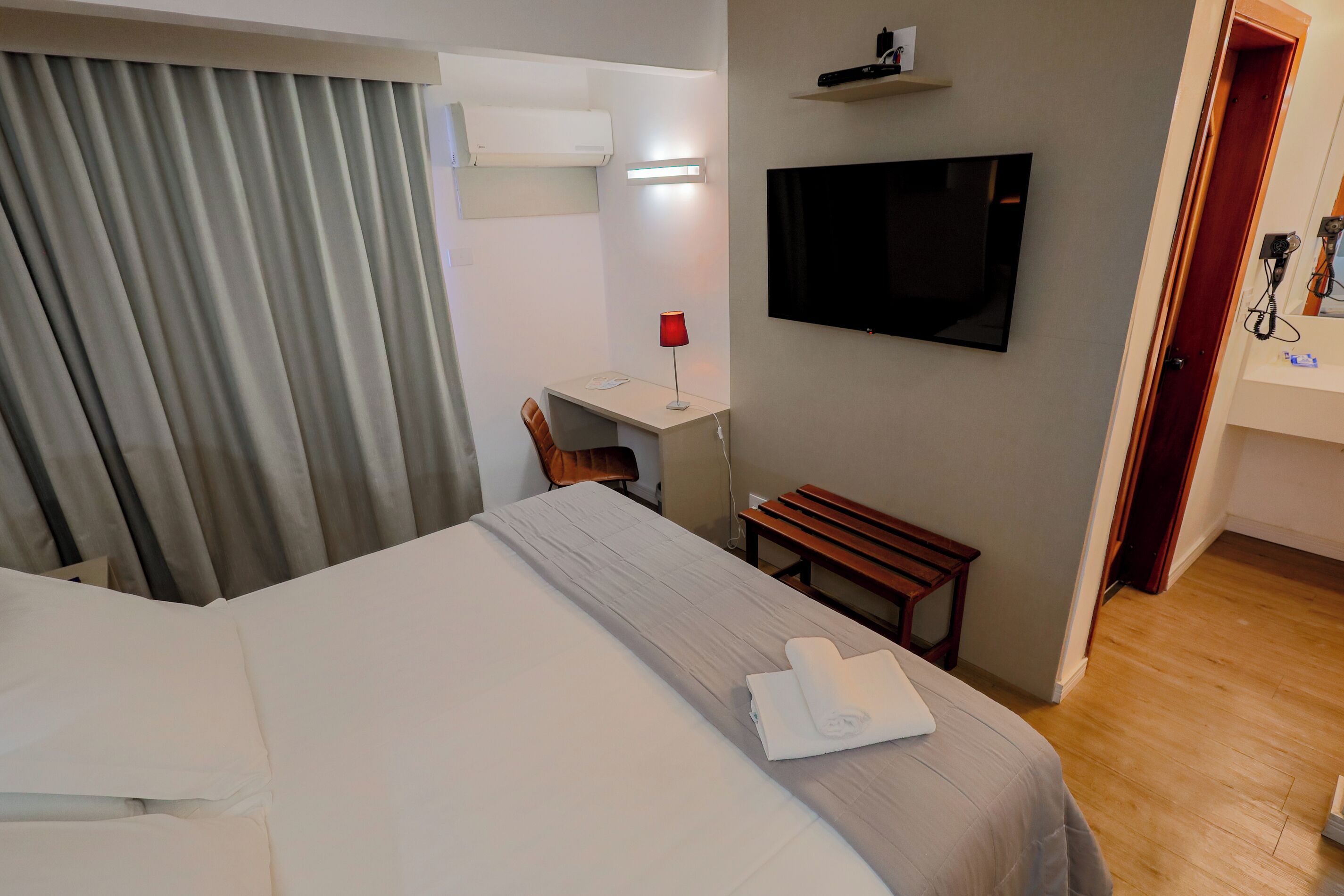 Ein Hotelzimmer mit einem Bett, einem Schreibtisch, einem Sessel, einem Fernseher und einer Holzbank.