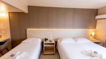 Quarto de hotel com duas camas de solteiro, cabeceira de madeira, mesas de cabeceira com luminárias e ar condicionado fixado na parede.