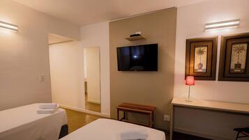 Habitación de hotel con dos camas, un televisor montado en la pared, una mesita y cuadros enmarcados.