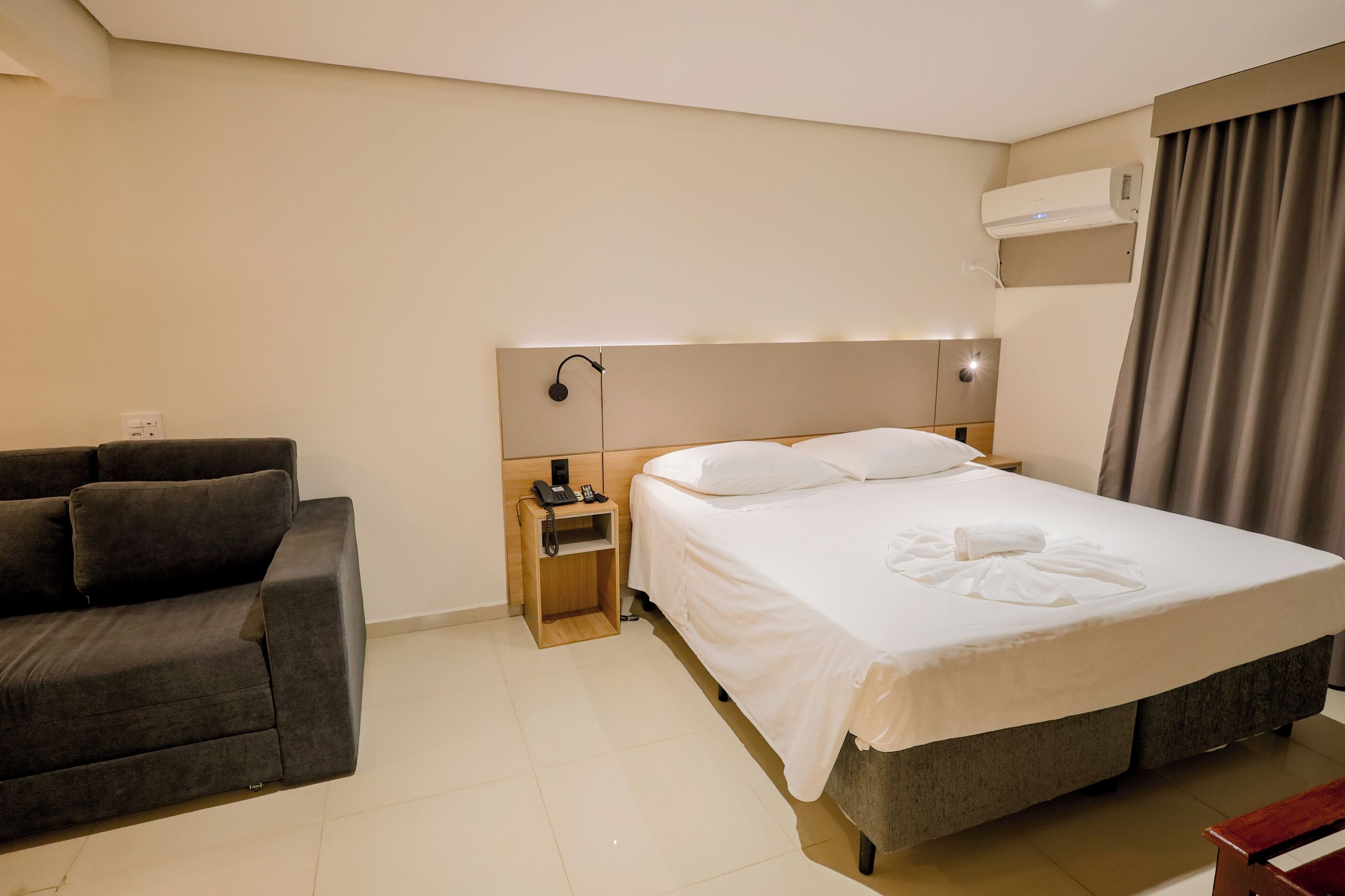 Une chambre d’hôtel équipée d’un lit, d’un canapé, d’une table de chevet avec un téléphone et d’un appareil de climatisation.