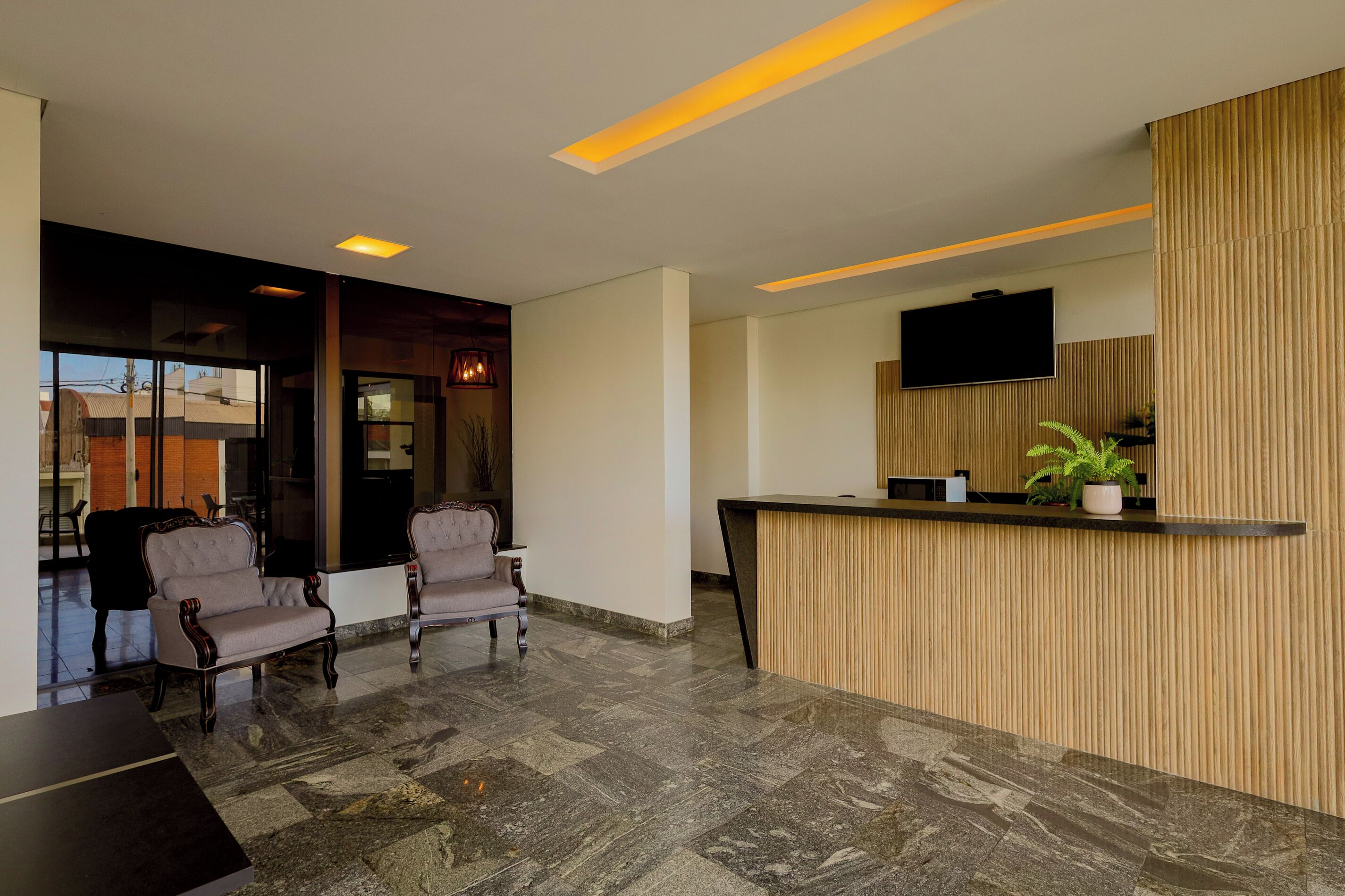 Un área de recepción moderna con un mostrador de madera, dos sillones tapizados y un televisor de pantalla plana montado en la pared.