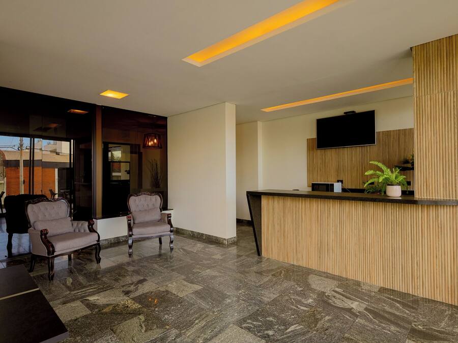 Un área de recepción moderna con un mostrador de madera, dos sillones tapizados y un televisor de pantalla plana montado en la pared.