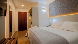 Una habitación de hotel con una cama grande, un banco de madera, un armario y un espejo.