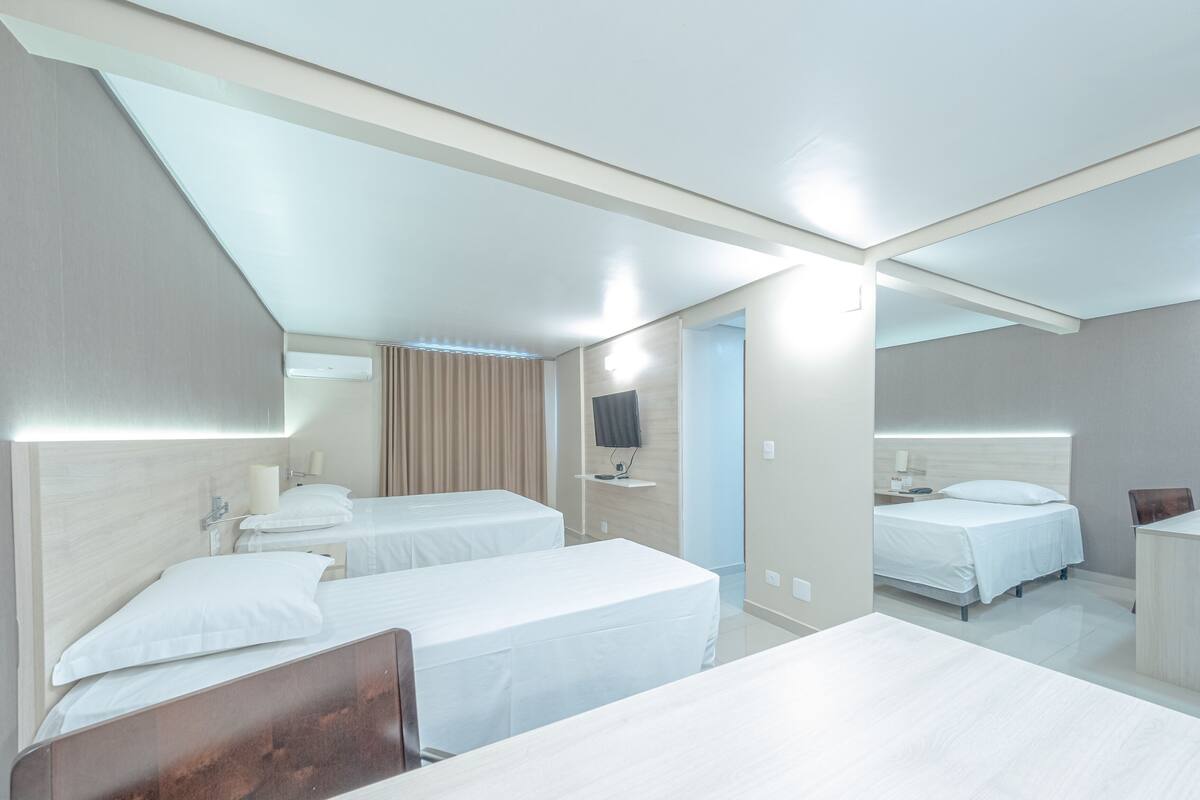 A hotel room with two beds, a desk, a mirror, a TV, and a bathroom.