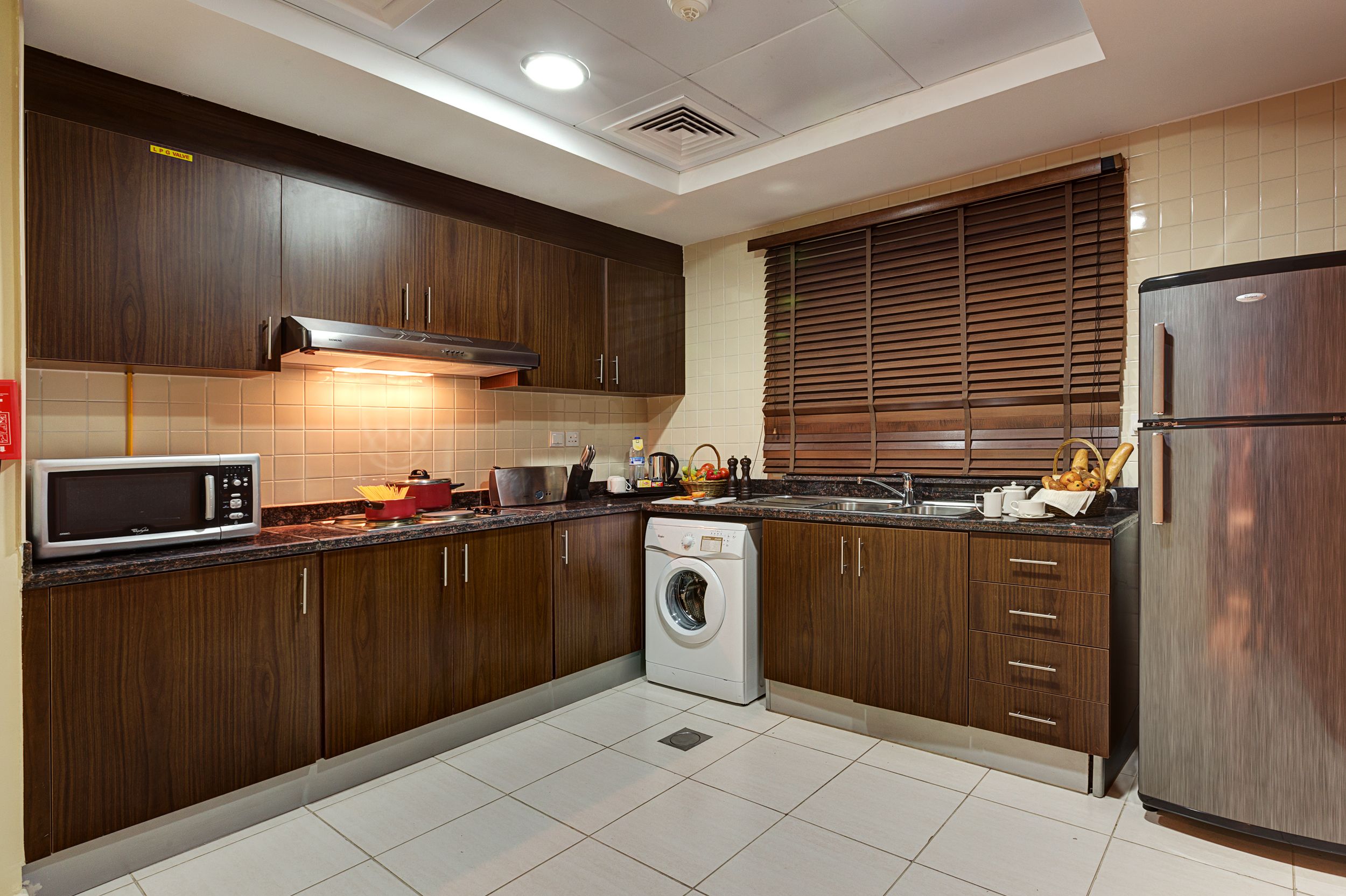 A modern kitchen with dark wooden cabinets, a stainless steel refrigerator, a washing machine, and a microwave.