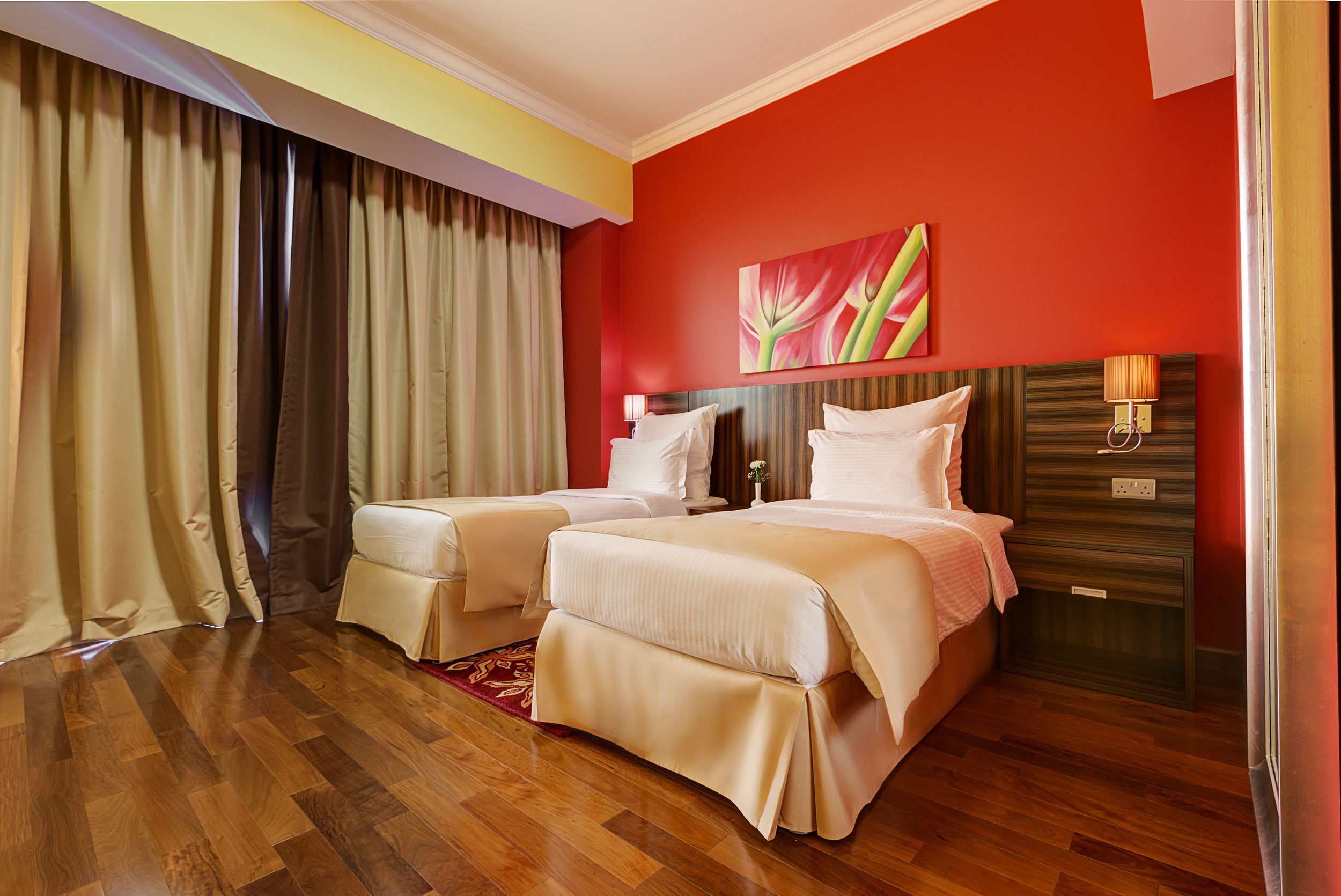 A hotel room with two beds, a red accent wall, and a wooden floor.