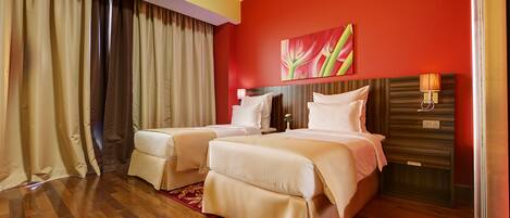 A hotel room with two beds, a red accent wall, and a wooden floor.