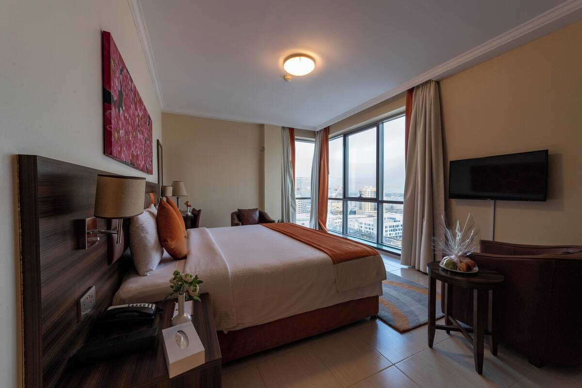 Habitación de hotel con una cama grande, televisión, escritorio y ventana con vista a la ciudad.