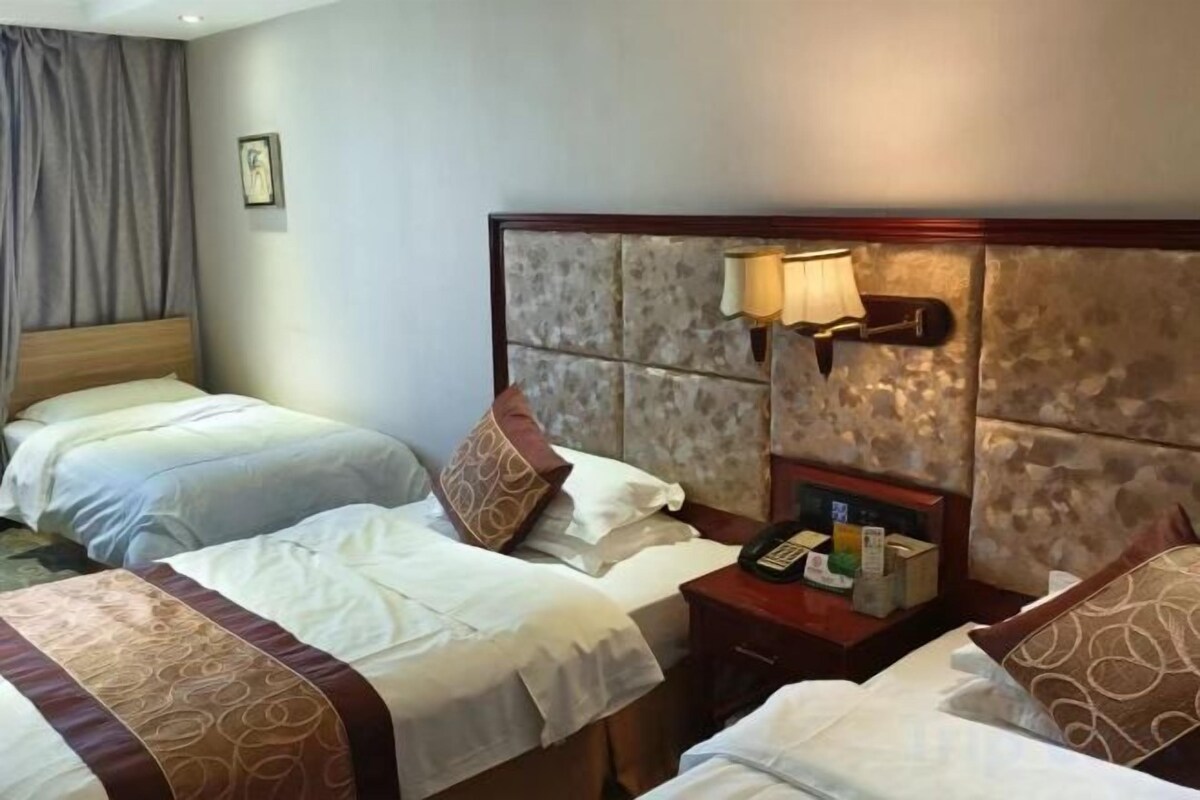 Una habitación de hotel con dos camas, una mesita de noche con lámpara y un teléfono instalado en la pared.