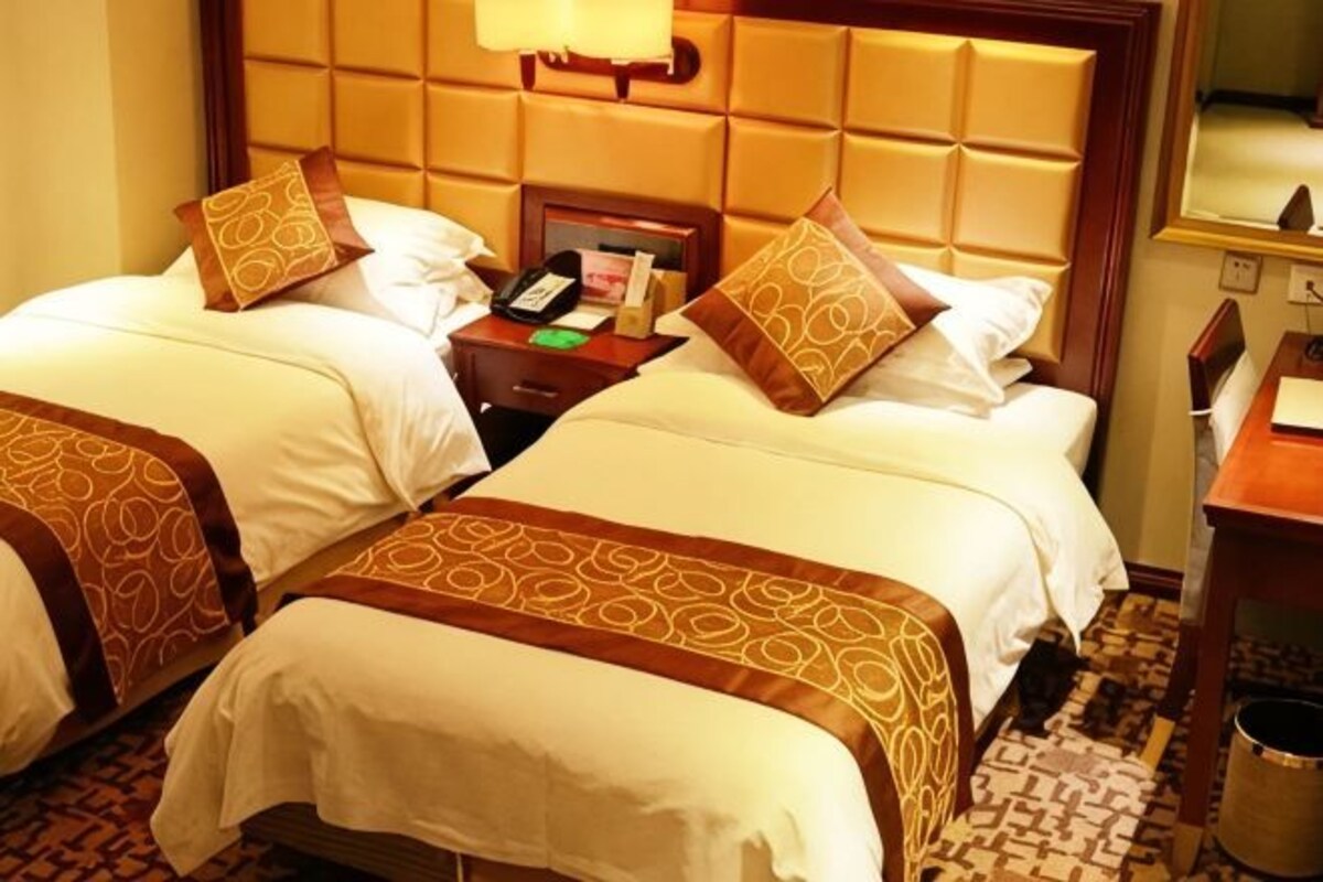 A hotel room with two beds, a nightstand, and a lamp.