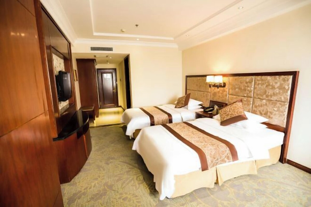 Una habitación de hotel con dos camas, un televisor y un armario de madera.