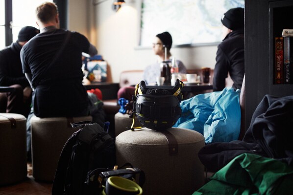 A group of people seated at a table in a room with luggage, suggesting a waiting area or lounge.