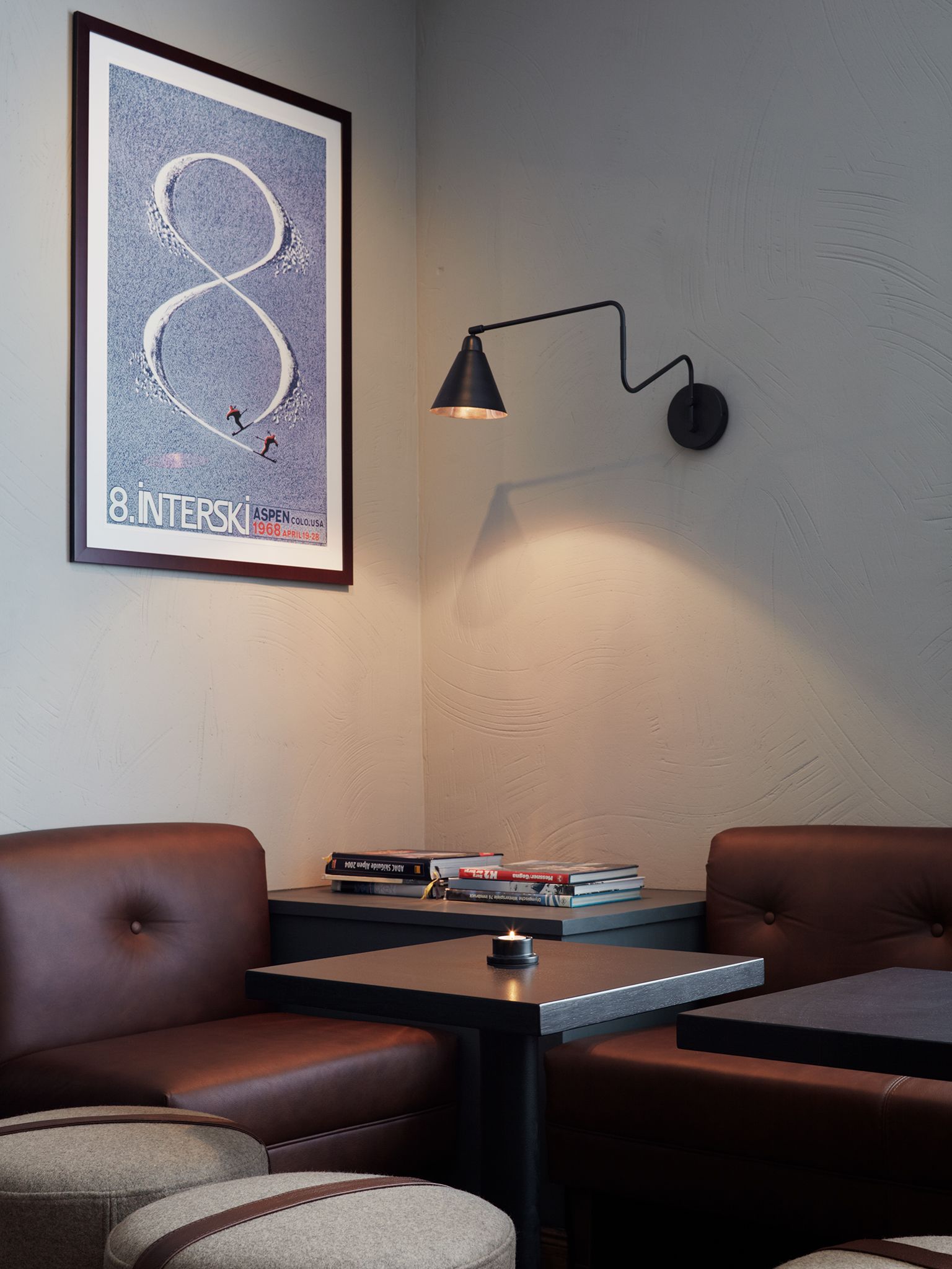 Una habitación moderna con sillones de cuero, una mesa con libros, un cartel enmarcado y una lámpara de pared.