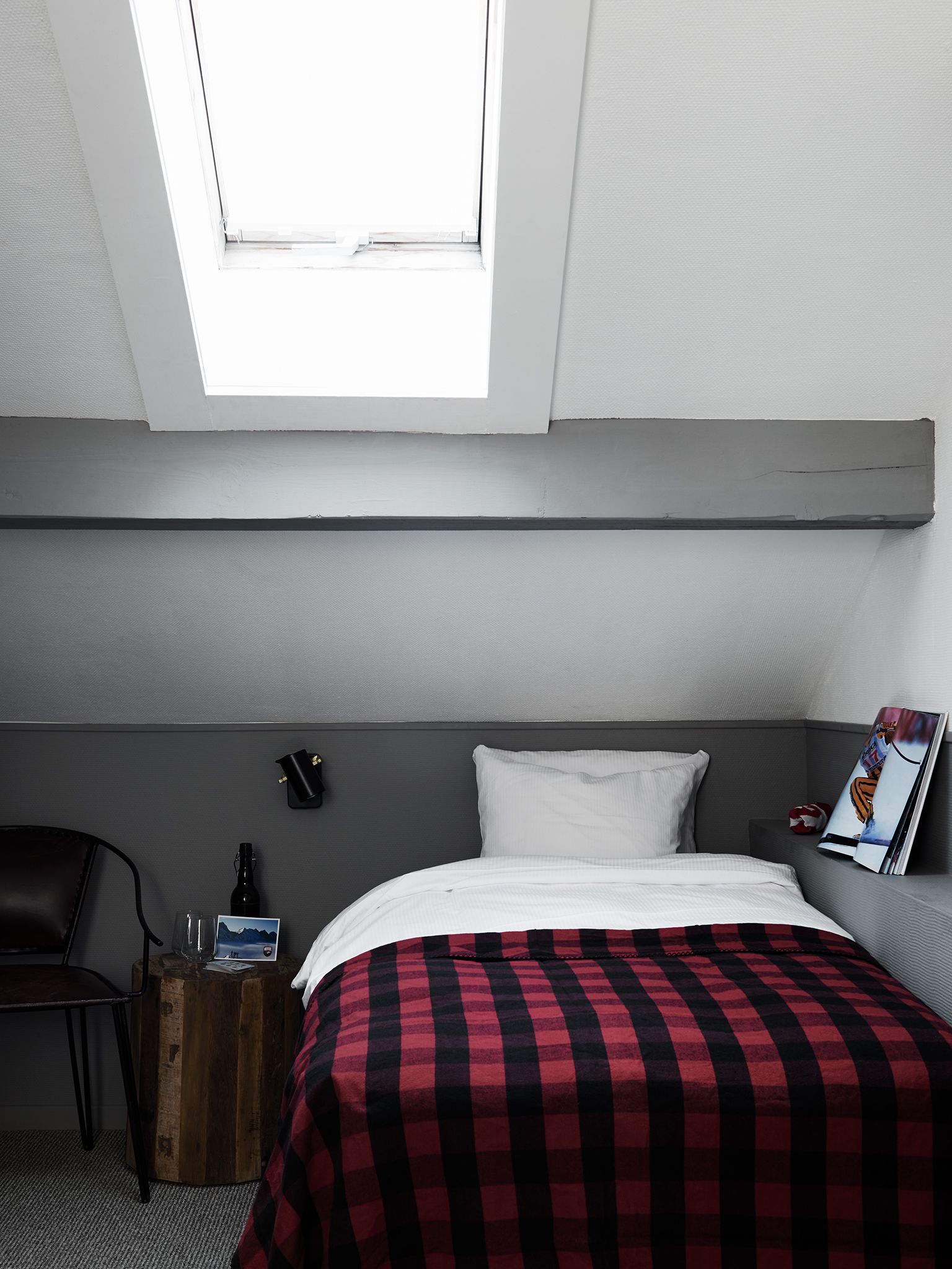 Habitación de hotel con una cama, una mesita de noche de madera, una silla, un buró, teléfono en la pared y ventana con vista al cielo.