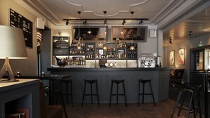 Un espace bar comprenant un comptoir, des tabourets, des étagères remplies de bouteilles et un tableau affichant le menu.