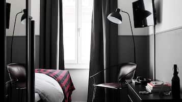 Una habitación de hotel con una cama, dos sillas, un escritorio con lámpara y una ventana con cortinas.